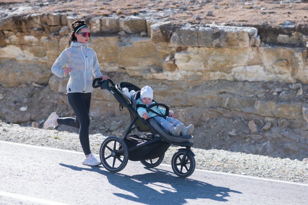 Madre corriendo con su bebé en un carrito por un camino al sol